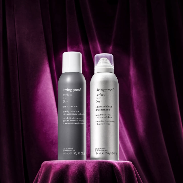 Two Living Proof dry shampoo bottles on a purple surface with a dark background