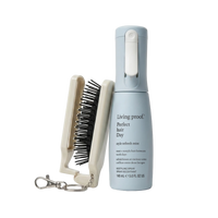 Living Proof Perfect Hair Day spray bottle in light blue next to a cream-colored hair brush with black bristles and a silver keychain clasp, on a white background.