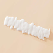 A wavy line of Curl Definer conditioning styler is spread on a smooth, light beige surface, suggesting frizz-free curls.