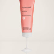 A pink 100 ml tube of Curl Definer conditioning styler dispenses a small amount of white product onto a flat surface for frizz-free curls. White text and a small logo appear on the tube.