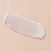 A smooth, white smear of Curl Enhancer with a creamy, slightly glossy natural texture is spread on a soft peach-colored background.