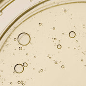Close-up of Curl Moisturizing Shine Oil’s transparent golden liquid with air bubbles, creating an abstract pattern that evokes hairs natural lipids against a light background.