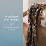 A person with long curly hair uses Clarifying Detox Shampoo in the shower. The text says: Weekly reset for all hair types—removes hard water buildup. Pair it with a conditioner or mask.