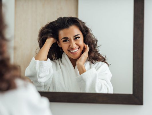woman smiling and fixing her hair in the mirror