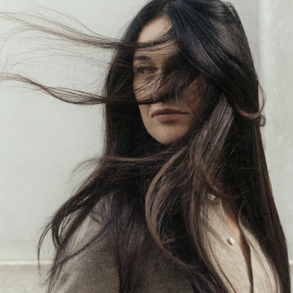 Woman with black hair blowing in the wind as she looks back.