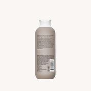 A beige bottle of No Frizz Smooth Styling Cream for medium hair with a white cap is shown from the back, featuring a label with frizz control benefits, ingredients, and a barcode. The background is plain off-white.