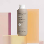 A bottle of No Frizz Smooth Styling Cream stands upright against pastel-colored translucent blocks, with a label stating it smooths and conditions medium hair.