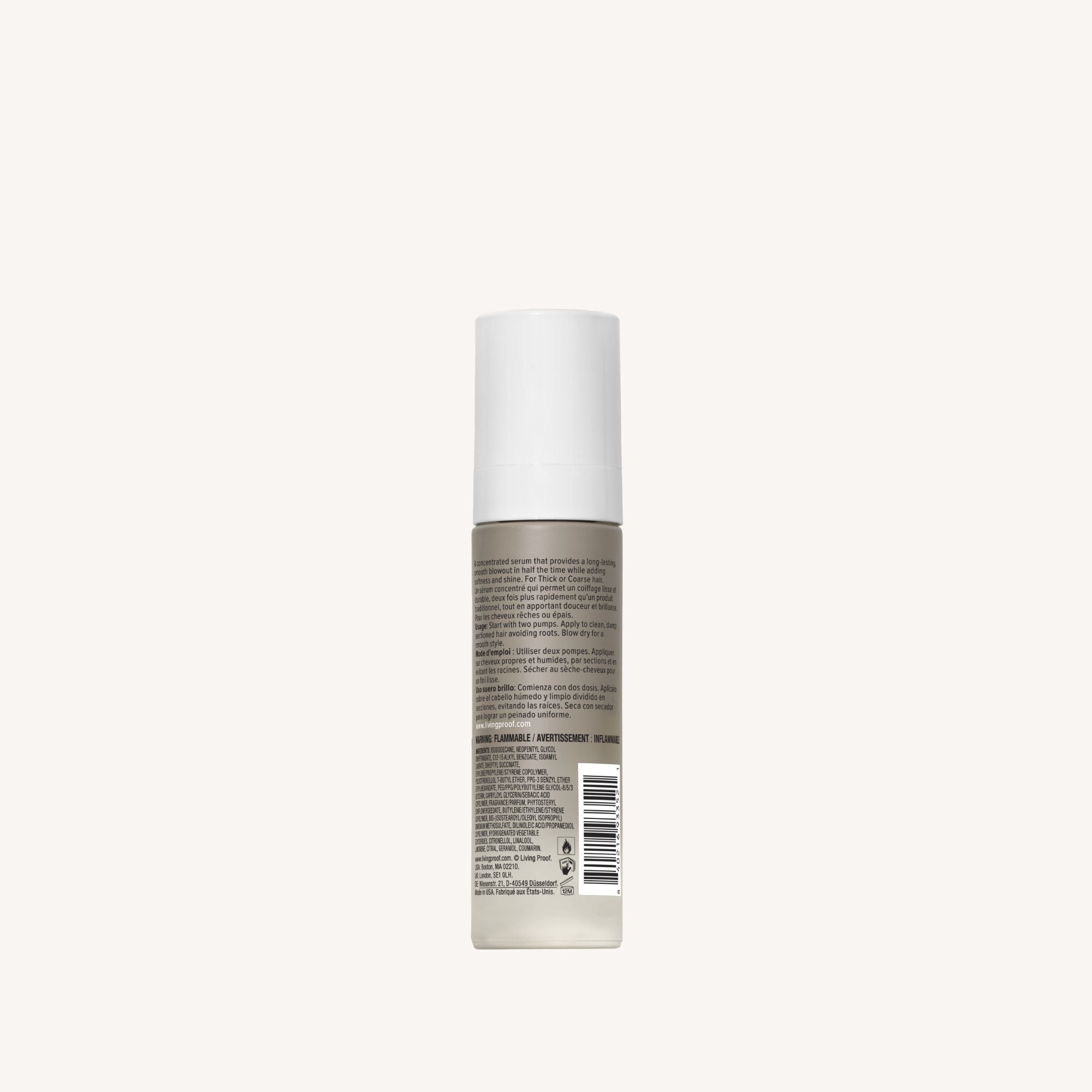 A small cylindrical bottle with a white cap stands upright. The label shows No Frizz Smooth Styling Serum, ideal for thick or coarse hair. Barcode is visible but unclear. Background is plain and light-colored.