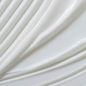Close-up of Full Thickening Blow-Dry Cream’s smooth white surface with curved ridges and grooves. Its glossy, reflective finish highlights the wavy, abstract pattern and soft texture of this styling product.