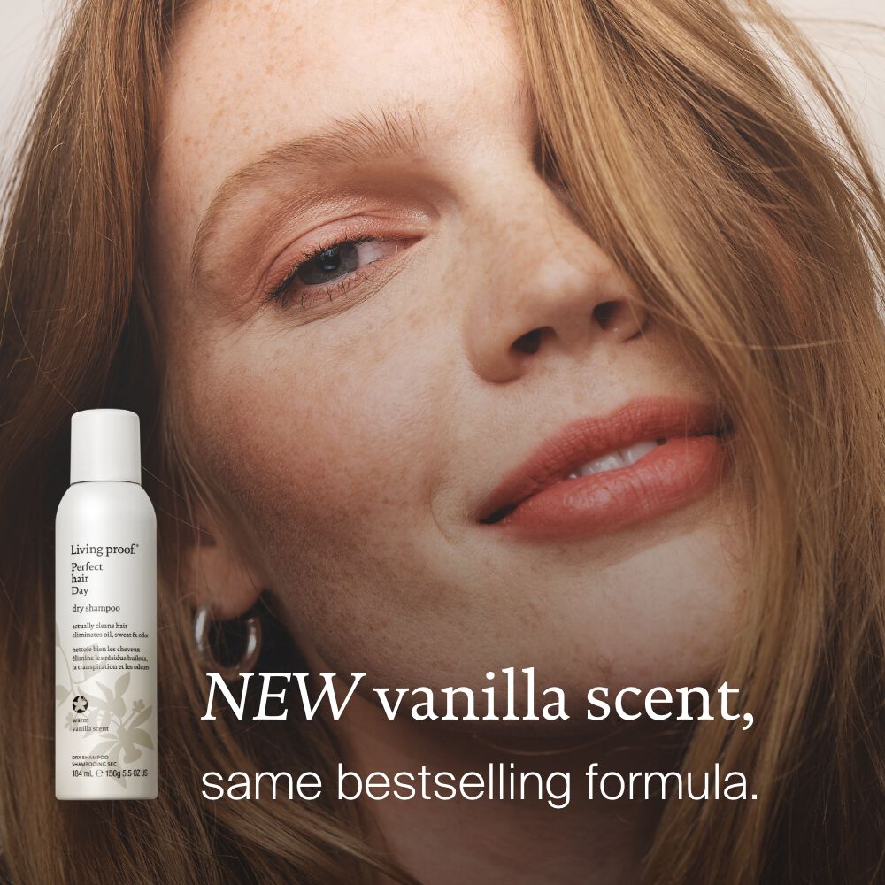 A red-haired woman with light makeup smiles softly. In the lower left, a bottle of Perfect hair Day™ Dry Shampoo - Limited Edition Vanilla is shown. Text reads: “NEW vanilla scent, same bestselling results for clean hair.”.