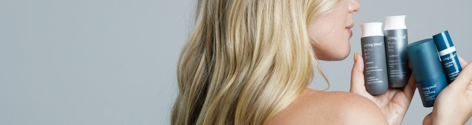 Woman holding hair care products against a neutral background