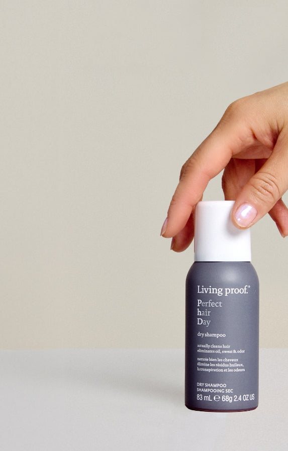 Hand holding a Living Proof shampoo bottle against a neutral background