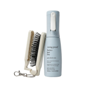 Living Proof Perfect Hair Day spray bottle in light blue next to a cream-colored hair brush with black bristles and a silver keychain clasp, on a white background.