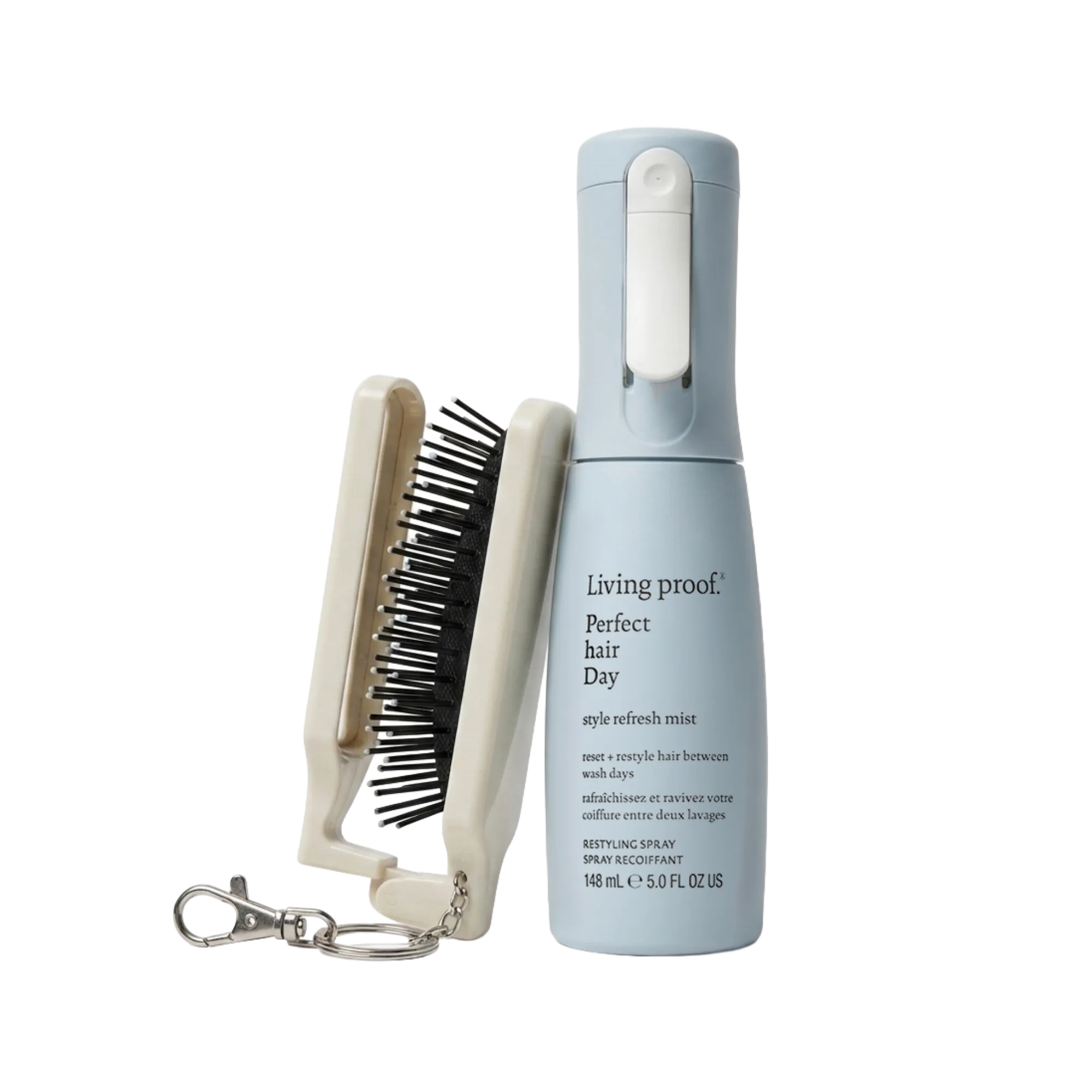 Living Proof Perfect Hair Day spray bottle in light blue next to a cream-colored hair brush with black bristles and a silver keychain clasp, on a white background.