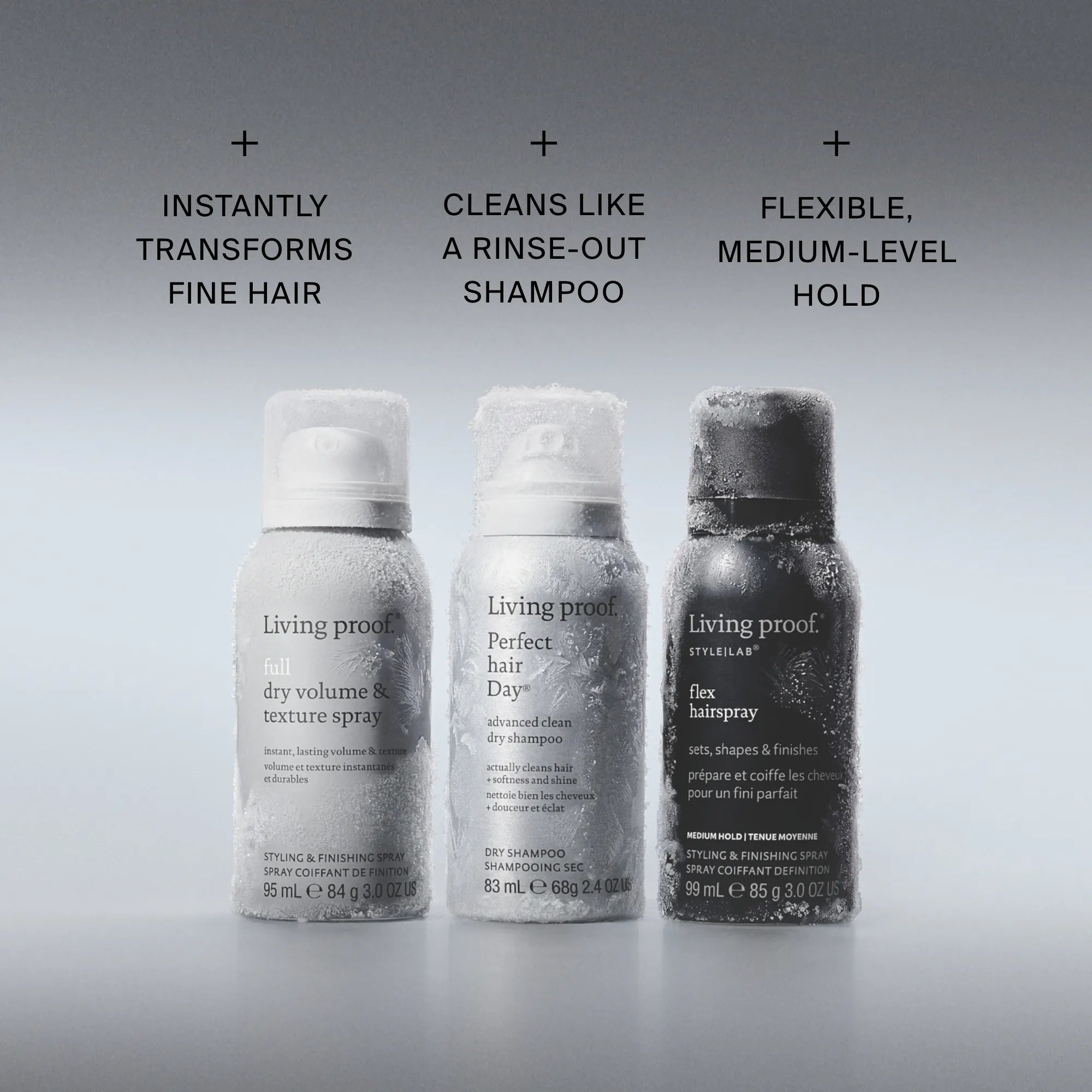 Three Living Proof hair product sprays—Flex Hairspray, Advanced Clean Dry Shampoo, and Dry Volume & Texture Spray from The Travel Essentials Set—stand lightly frosted side by side on a grey background with their descriptions displayed above: volume/texture spray, dry shampoo, and flex hairspray.