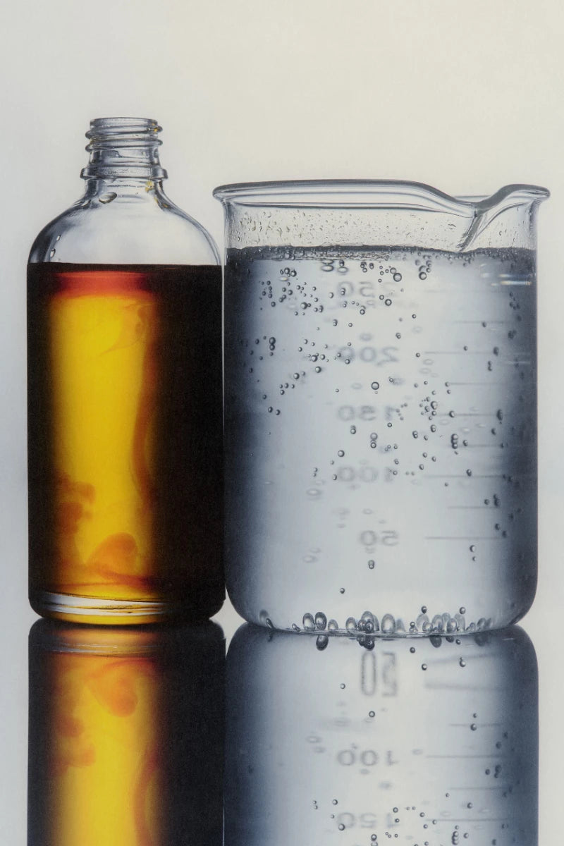 Bottle of amber liquid next to a beaker with water on a reflective surface