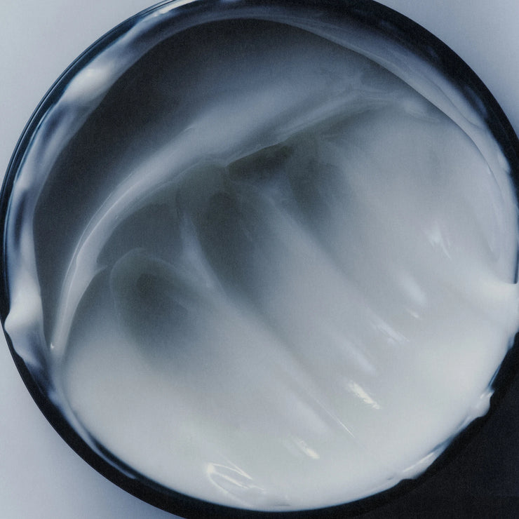 Close-up of a container of white cream or gel with a black lid.