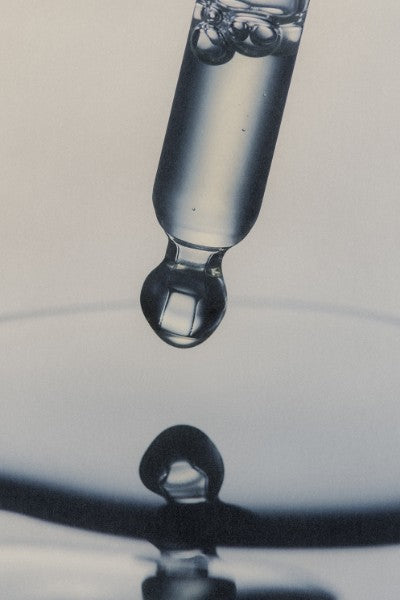 Close-up of a dropper with liquid being dispensed onto a reflective surface.