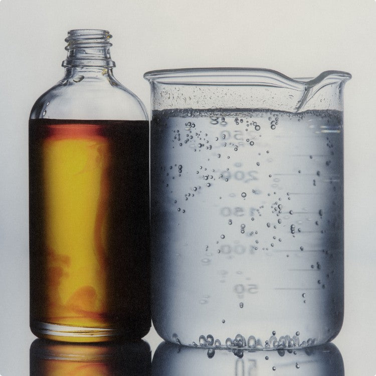 Clear bottle with amber liquid next to a beaker with bubbling clear liquid on a light gray background