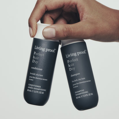 Hand hold up two bottles of travel sized living proof perfect hair day shampoo and conditioner