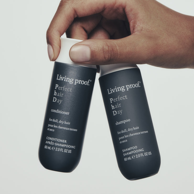 Hand hold up two bottles of travel sized living proof perfect hair day shampoo and conditioner