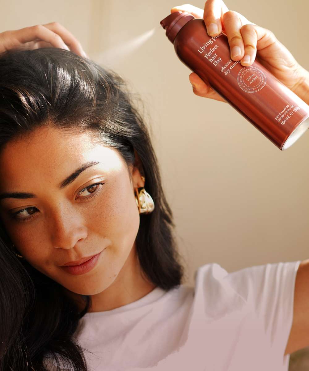 Person applying hair product from a red bottle to their hair