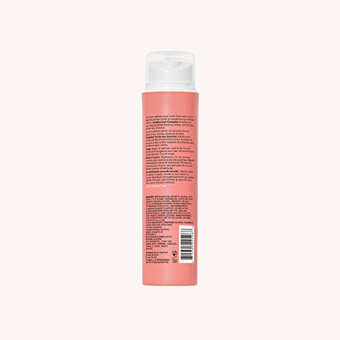 A tall, cylindrical, coral-colored bottle with a white pump dispenser. The back label of Curl Definer details its frizz-free curl conditioning formula, ingredients, product info in small text, and has a barcode at the bottom.