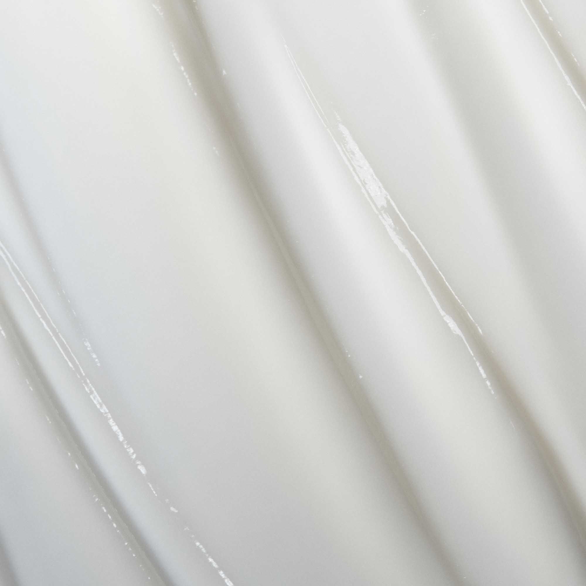 Close-up of the smooth, glossy white surface of Curl Conditioner, featuring gentle vertical ridges and curves—evoking defined curls after hydration—and reflecting soft light.