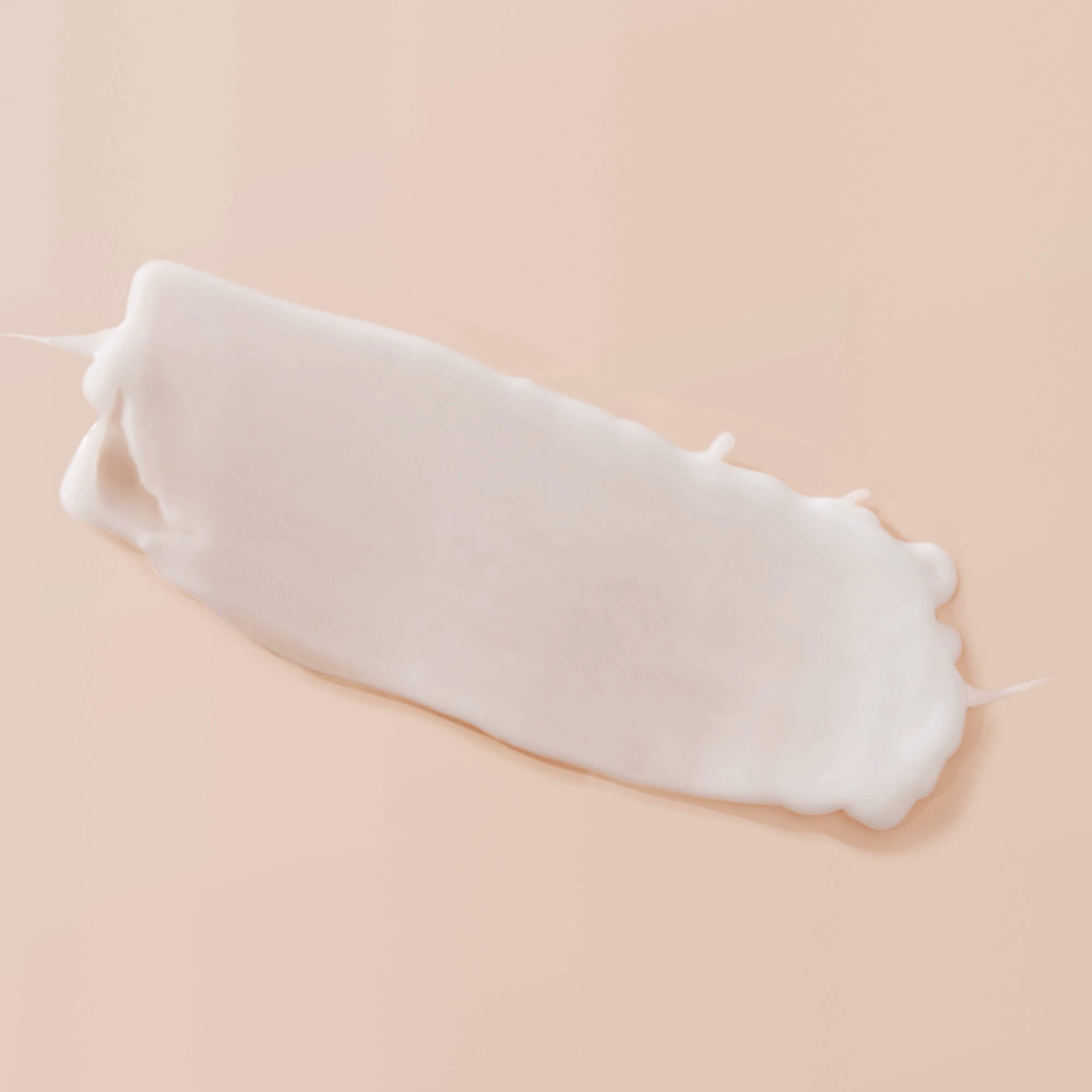 A smooth, white smear of Curl Enhancer with a creamy, slightly glossy natural texture is spread on a soft peach-colored background.