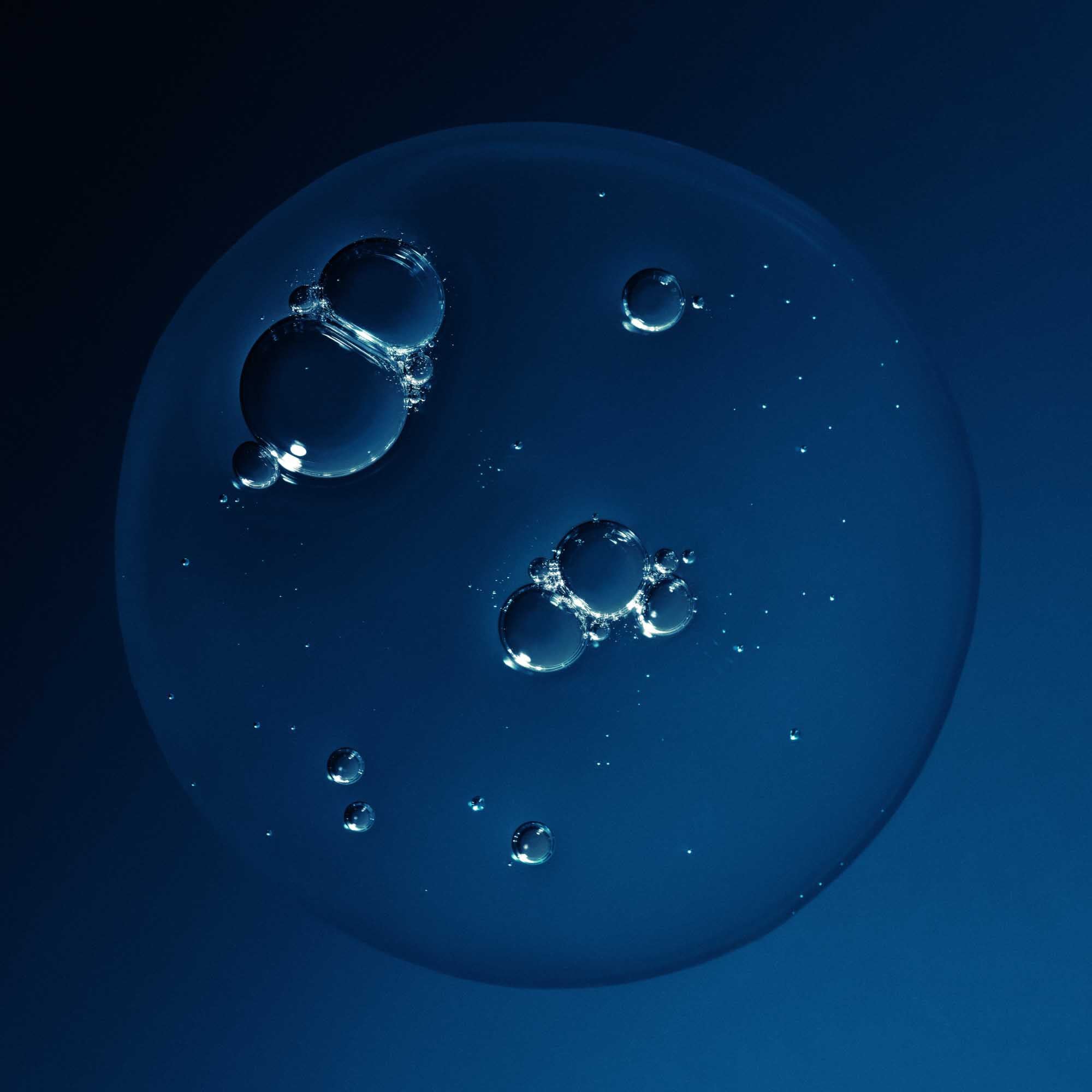 A cluster of transparent bubbles floats against a dark blue background, illuminated by light that highlights their glossy surfaces—evoking the refreshing, volumizing effect of a Full Shampoo + Refill experience.