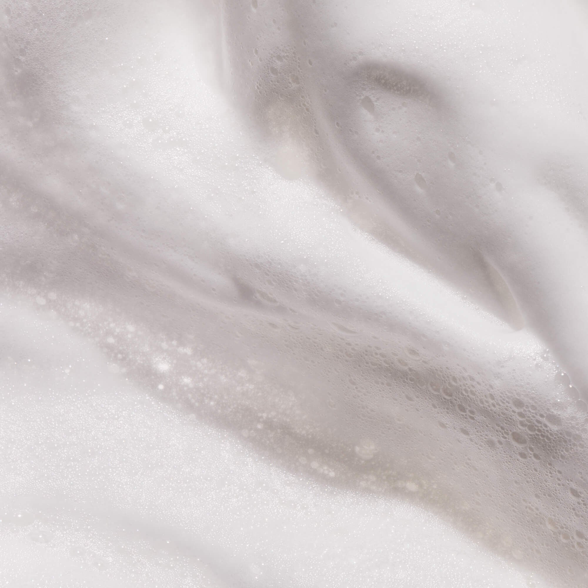 Close-up of Full Thickening Mousse reveals dense, creamy white foam with a cloud-like texture. The voluminous bubbles highlight the mousse’s ability to create impressive body and smooth fullness, enhanced by gentle highlights and shadows.