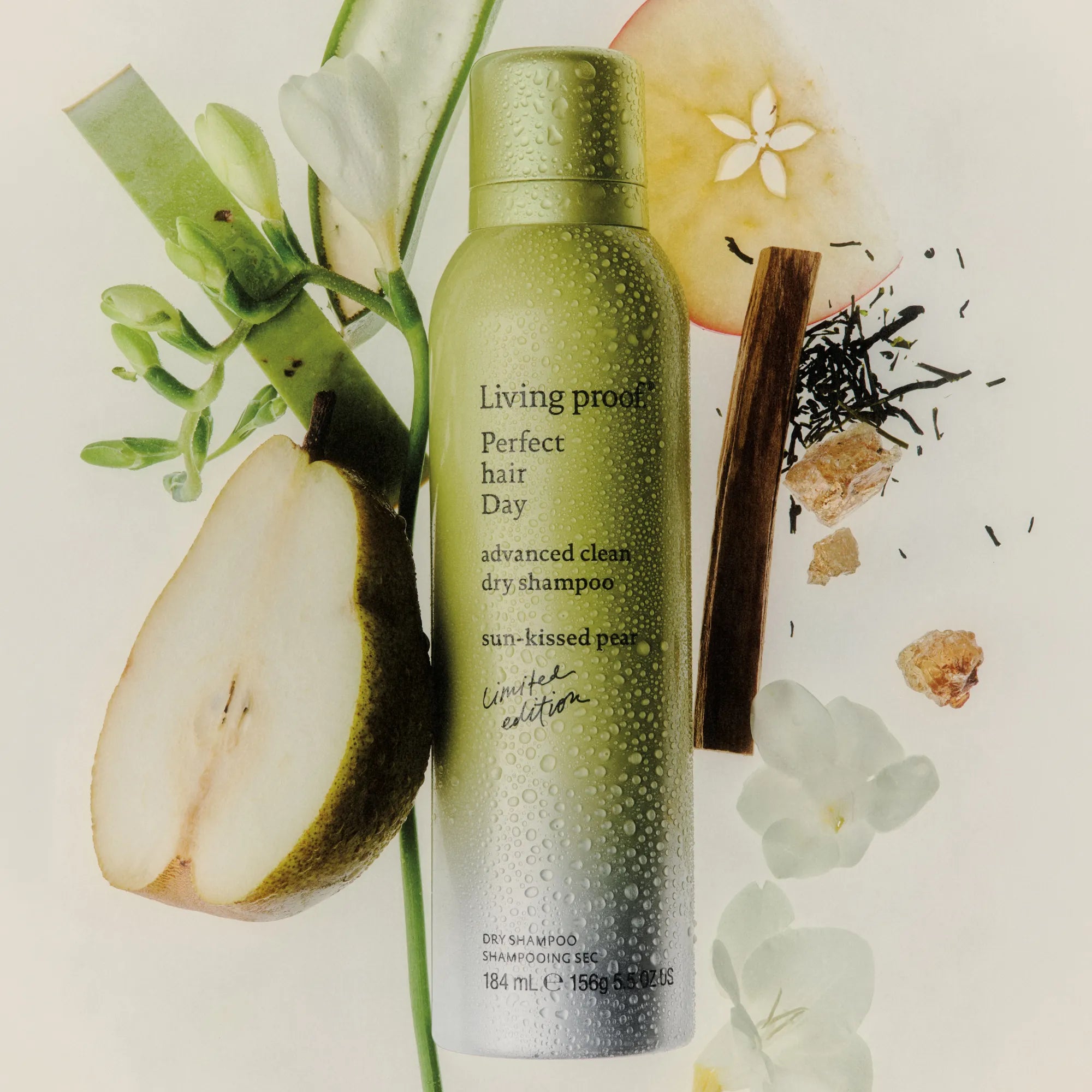 Living Proof dry shampoo bottle with pear and floral elements on a light background