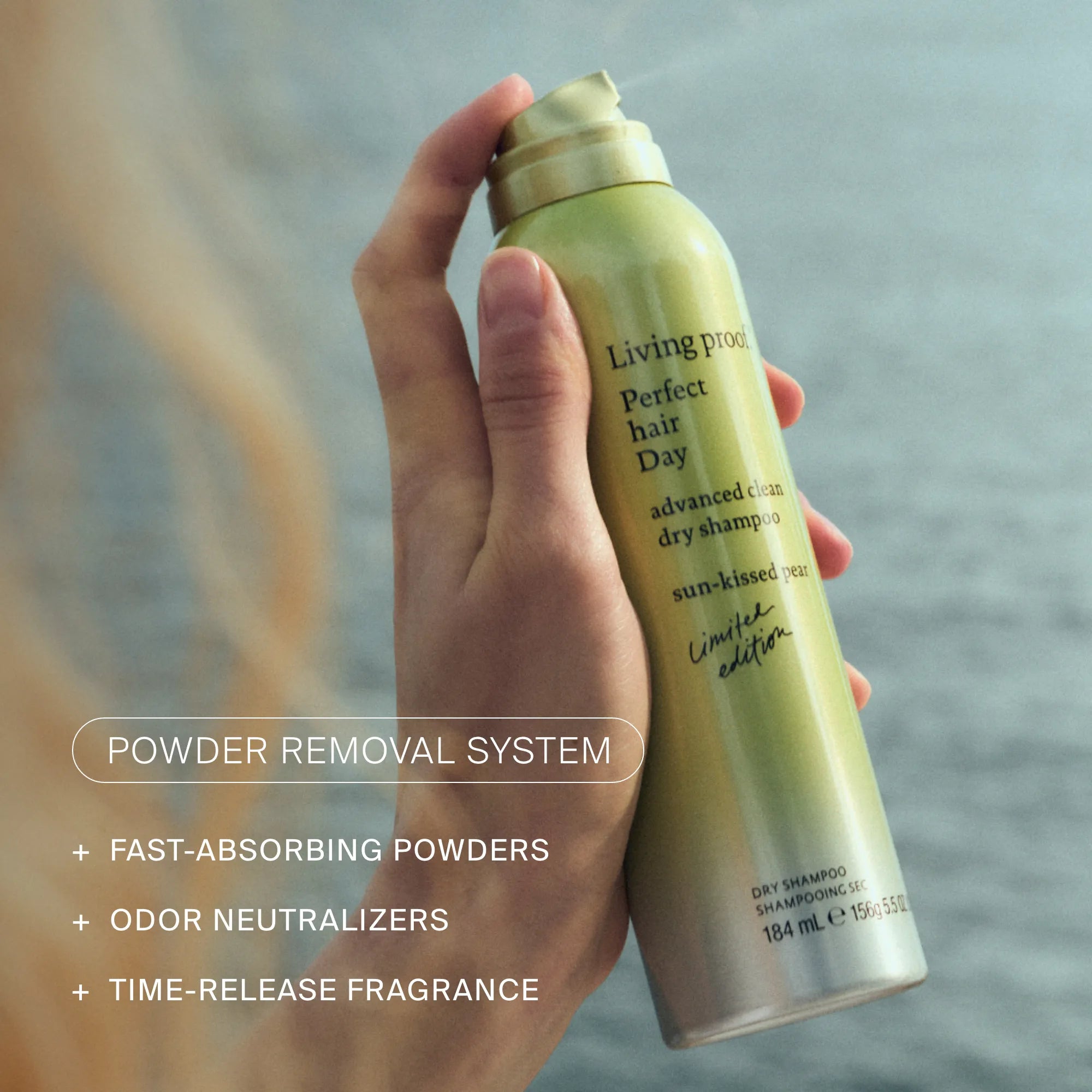 Hand holding a green bottle labeled 'Living Proof' with text about a powder removal system.