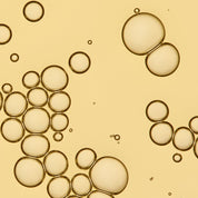 Close-up image of translucent bubbles in various sizes clustered on a yellowish background, resembling hydrating No Frizz Vanishing Oil droplets suspended in liquid.