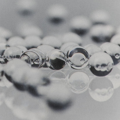 Clear glass marbles or beads scattered on a reflective gray surface, with shallow depth of field focusing on the foreground beads.
