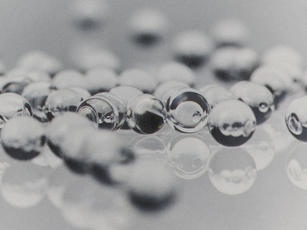 Clear glass marbles or beads scattered on a reflective gray surface, with shallow depth of field focusing on the foreground beads.