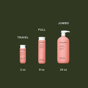 Three pink bottles of Curl Shampoo in travel (2 oz), full (8 oz), and jumbo (24 oz) sizes, each labeled with its size, are displayed on a dark green background. This silicone-free shampoo enhances curls beautifully.