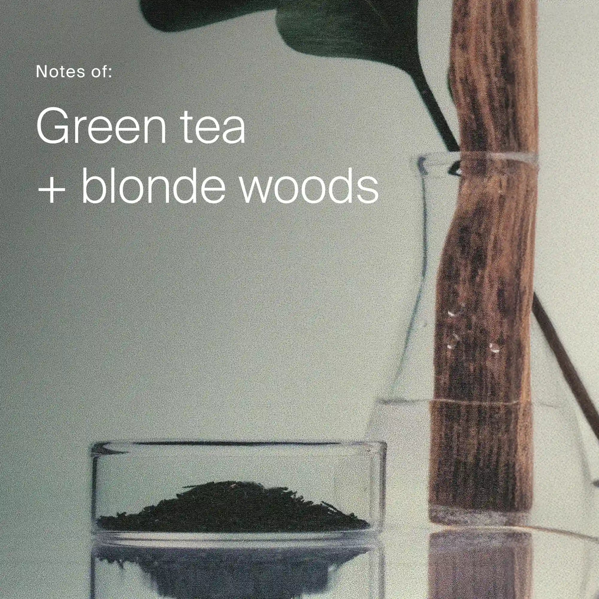 Glass with green tea leaves and wooden spoon on a light gray background with text 'Notes of: Green tea + blonde woods'.