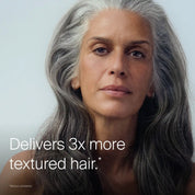 A woman with long, thick, gray hair and a calm expression looks at the camera. Text reads, "Full Texturizing Foam: Delivers 3x more hair texture*". Small text underneath says, "*versus untreated.