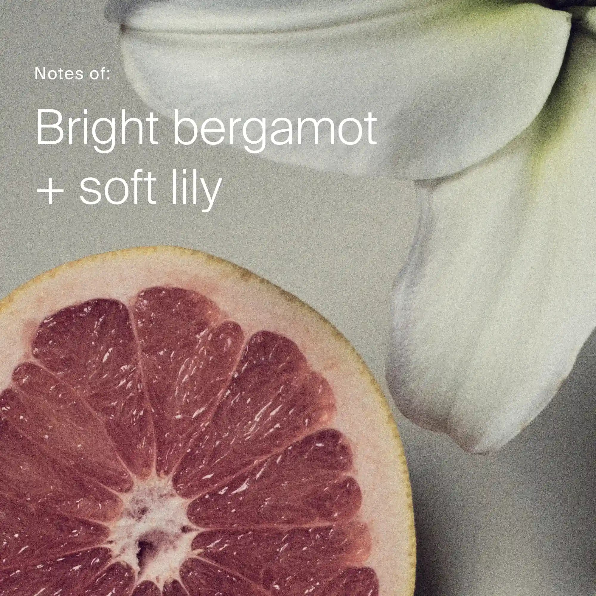Close-up of a pink grapefruit and a white lily with text 'Notes of: Bright bergamot + soft lily' on a gray background.