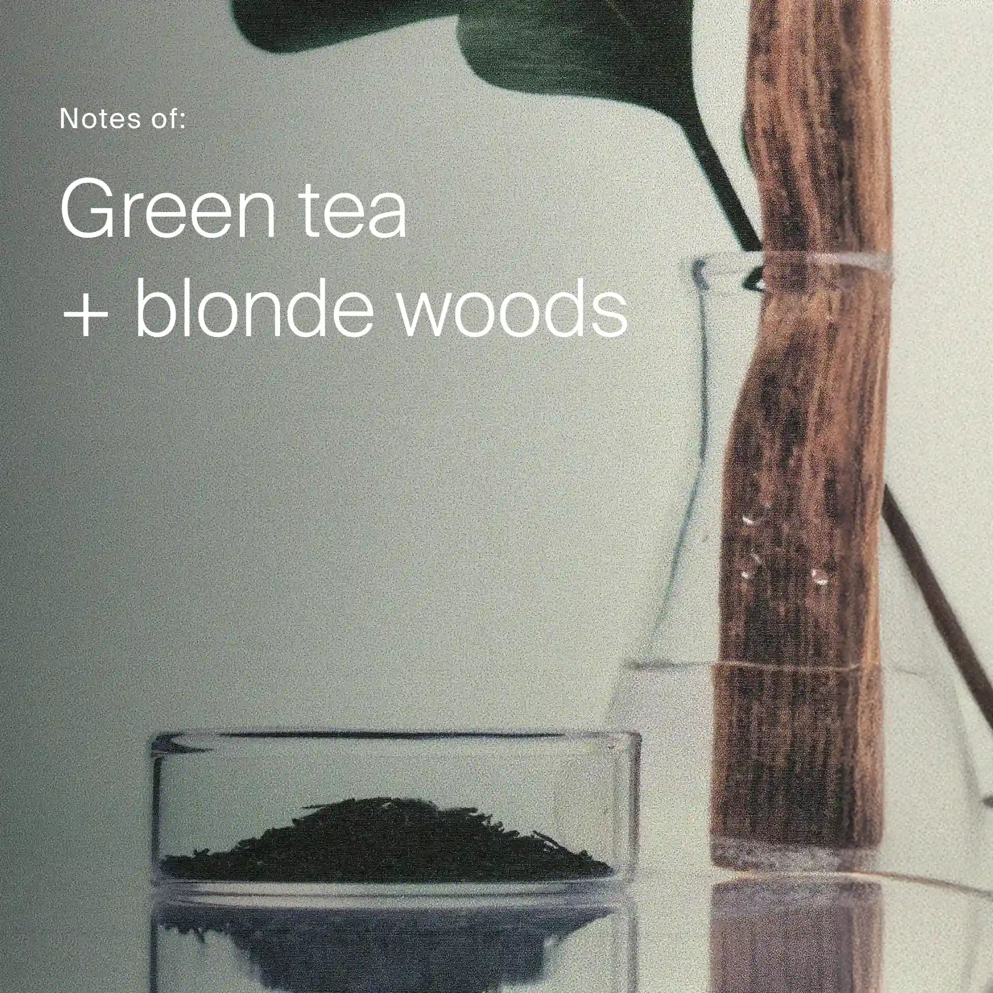 Glass container with green tea leaves and wooden spoon on a light background, with text 'Notes of: Green tea + blonde woods'.