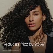 A woman with voluminous, curly hair looks at the camera against a plain background. The text reads, "Reduces frizz by 95%*." Small print notes use of the Curl Definition + Moisture Set for frizz-free curls.