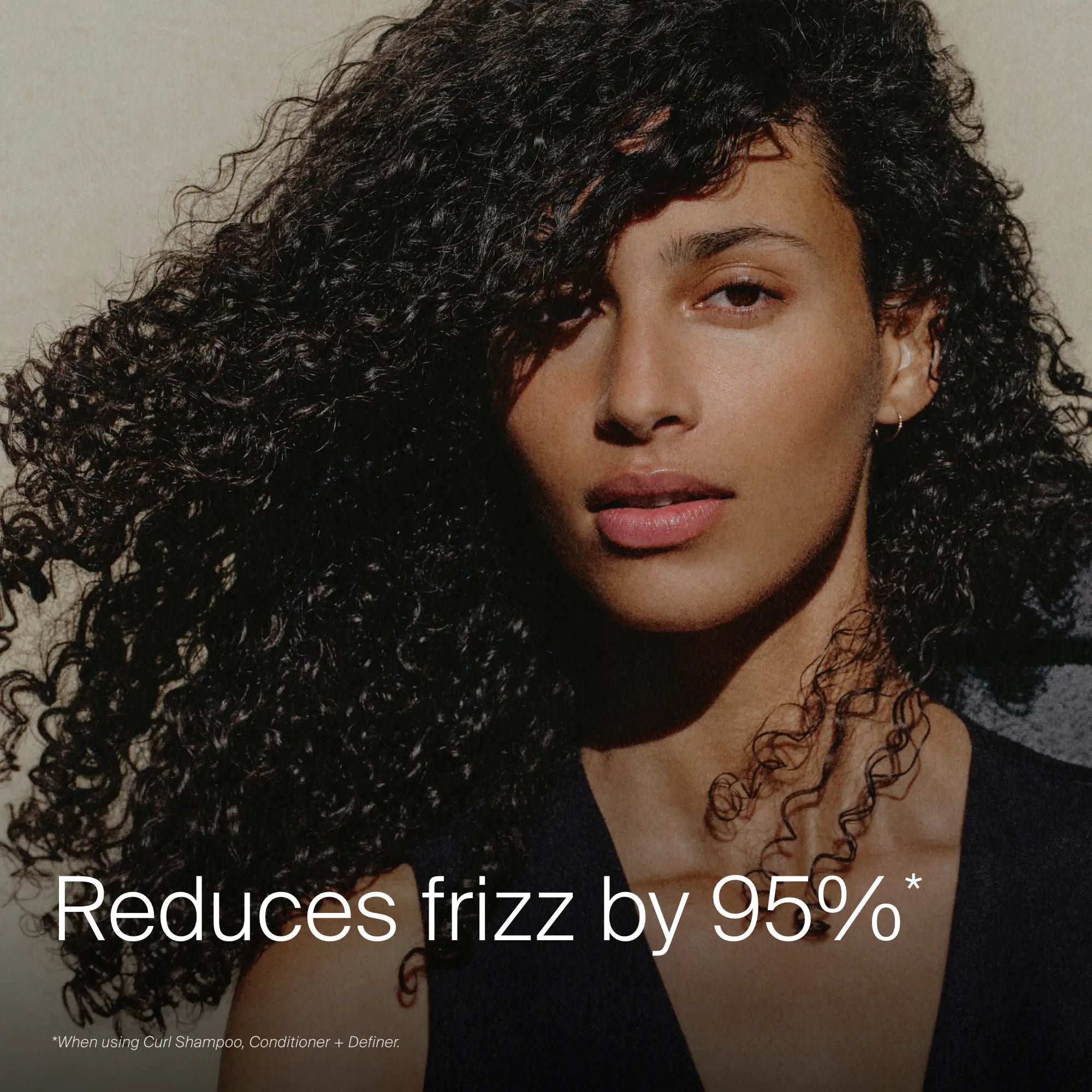A woman with voluminous, curly hair looks at the camera against a plain background. The text reads, "Reduces frizz by 95%*." Small print notes use of the Curl Definition + Moisture Set for frizz-free curls.