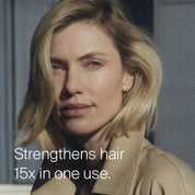 A woman with blonde, shoulder-length hair looks at the camera, wearing a beige coat. White text reads: Strengthen your hair 15x in one use with Restore Repair Leave-In.