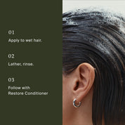 Close-up of a person’s wet hair with Restore Wash Duo shampoo lather beside text: 1. Apply to wet hair, 2. Lather, rinse, 3. Follow with Restore Conditioner. Person wears a silver hoop earring.