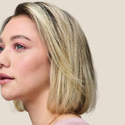 A woman with short, straight blonde hair and a side part, showing off shine and softness from using Restore Repair Mask, wears light pink makeup and a pink top while looking slightly to the left against a plain beige background.