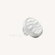 The Scalp Care Massager is a white silicone tool with pointed bristles, a round handle, and a hanging loop, designed for scalp exfoliation and shown against a plain light background.
