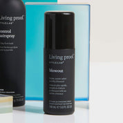 A black bottle of Style Lab® Blowout styling spray stands upright, with a blue box and another Living Proof item partially visible in the background—perfect for achieving a long-lasting blowout.
