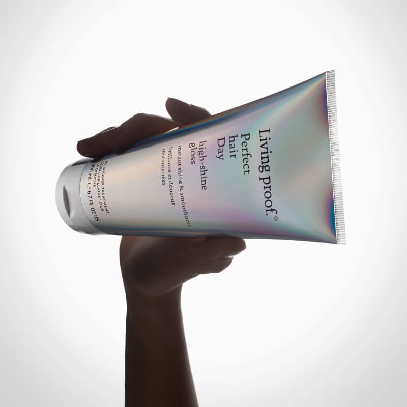Living Proof hair product tube held by a hand on a white background