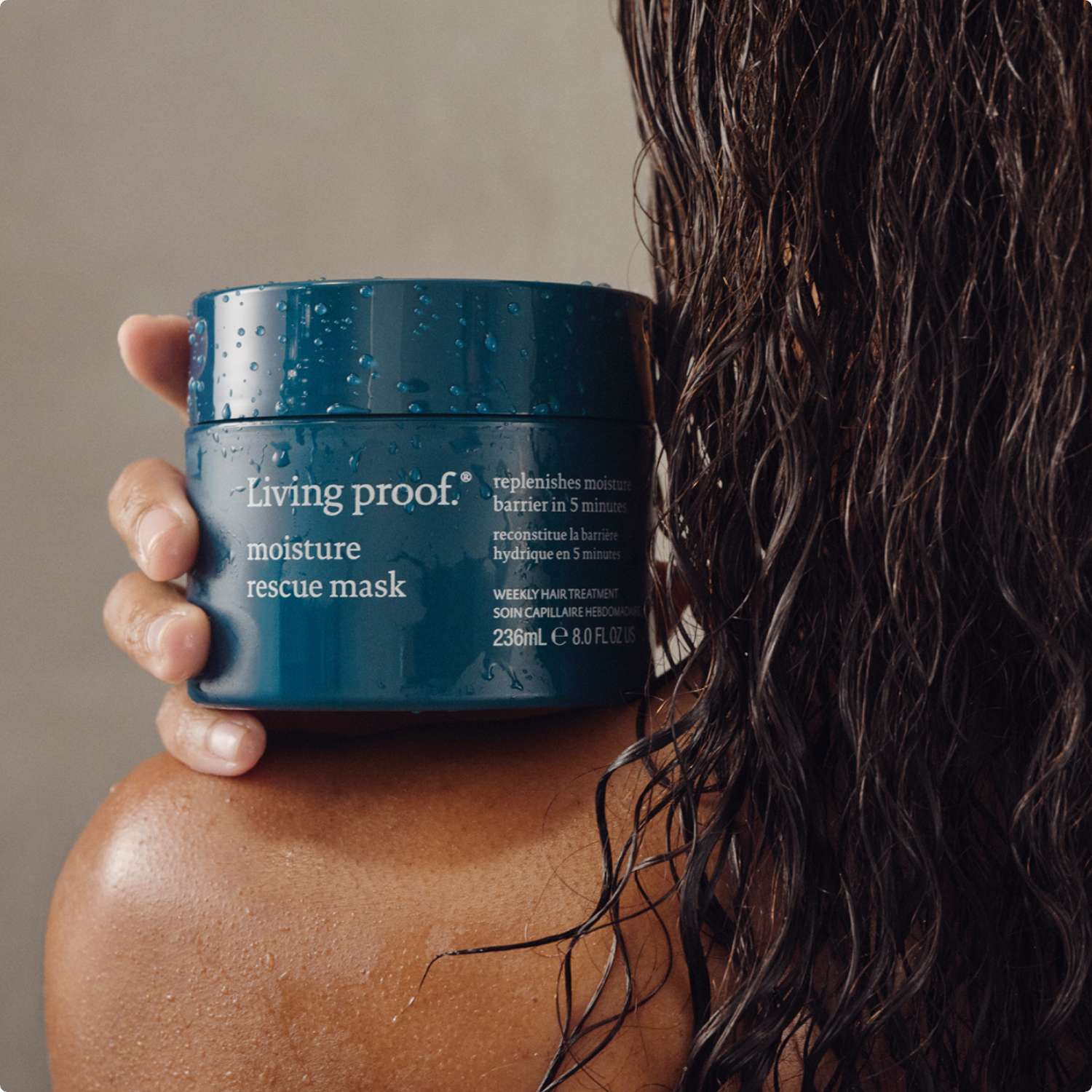 Person holding a jar of Living Proof moisture rescue mask with wet hair.